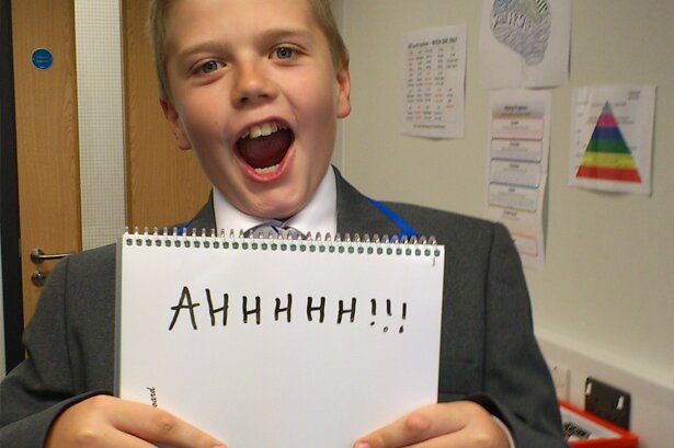 Picture of boy pretending to scream, holding a placard saying AAAAAAH!